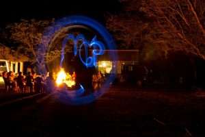 Volunteers gathered around a bonfire at night, with a light-painting photo effect spelling out MCP