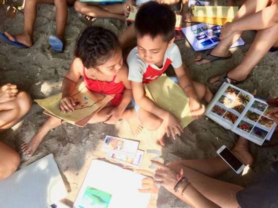 Local children on the beach looking at marine life picture cards