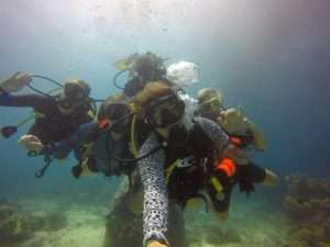 Group of divers posing for an underwater selfie, giving OK hand signs