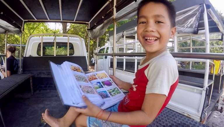 A local boy smiling while looking through a marine life picture book in the back of a truck