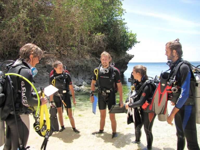Group of divers in wetsuits gathered on a rocky beach for a dive briefing