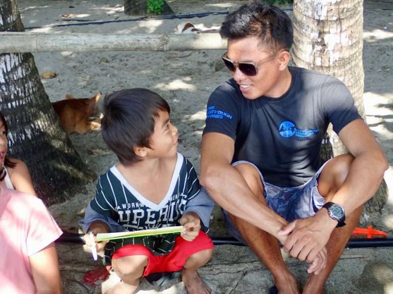 A staff member sitting and talking with a local boy during a youth education activity