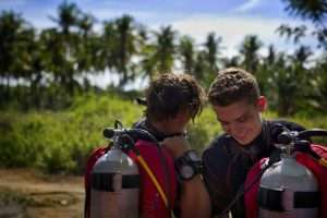 Two divers in scuba gear laughing together before a dive