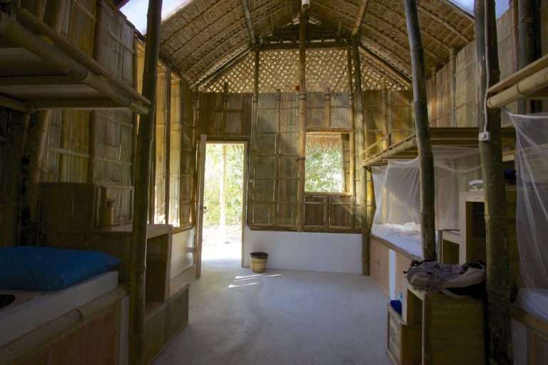 Interior of a bamboo-walled volunteer dorm room with bunk beds and mosquito nets
