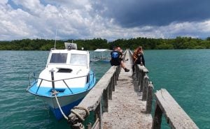 A dive boat moored beside a long concrete jetty, with divers walking out