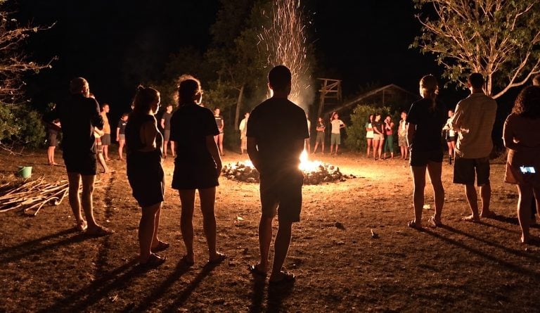 Sea Camp participants standing around an evening campfire