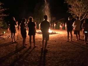Volunteers and local youth gathered around a bonfire at night during Sea Camp