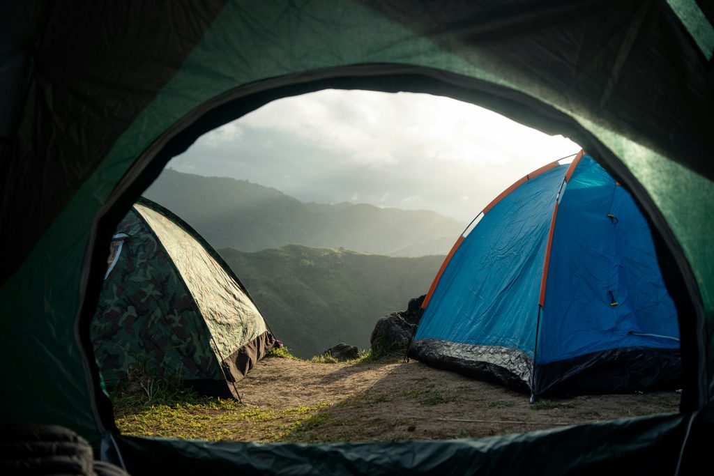 View from inside a tent of two more tents pitched on a mountain ridge, with forested hills in the morning light