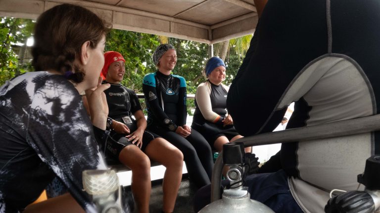 Smiling volunteer divers in wetsuits riding in the back of the MCP truck