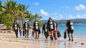 Divers in full scuba gear walking across the beach towards the water