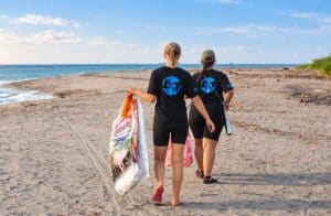 Two volunteers walking along the beach with bags of collected rubbish