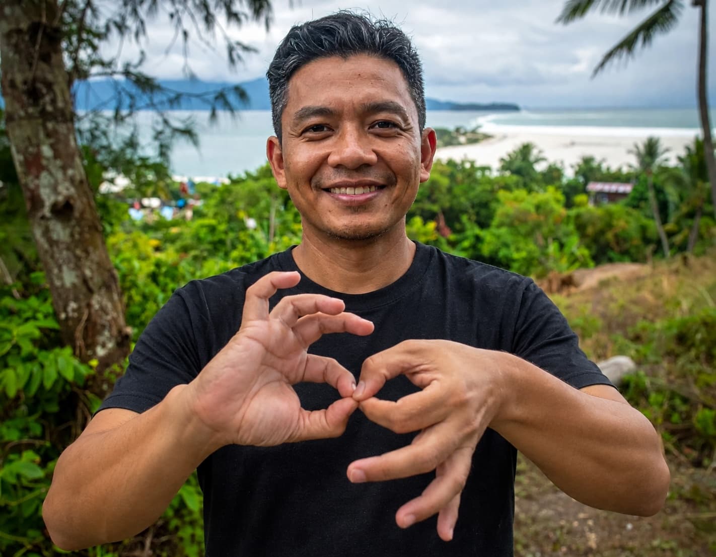 Smiling MCP team member making a hand sign, with the coastline behind him