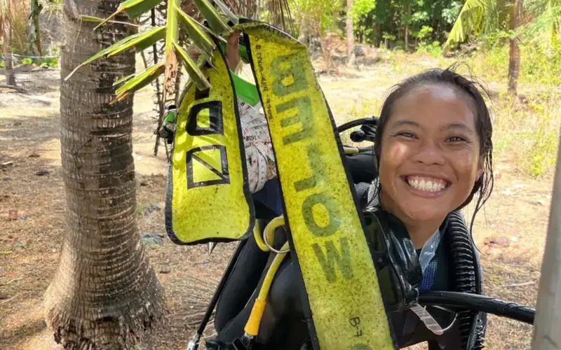 An MCP scholar smiling in scuba gear among palm trees
