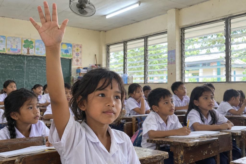 A girl raising her hand in a Philippine classroom, with classmates at their desks behind her