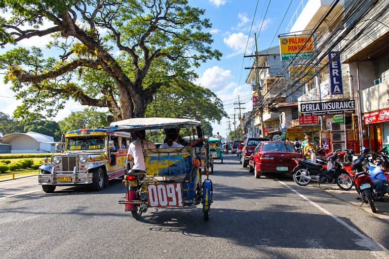 A jeepney and a tricycle on a tree-lined street in Dumaguete