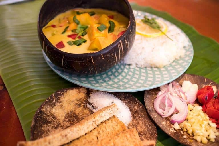 Pumpkin curry in a coconut shell bowl, with rice and side dishes on a banana leaf